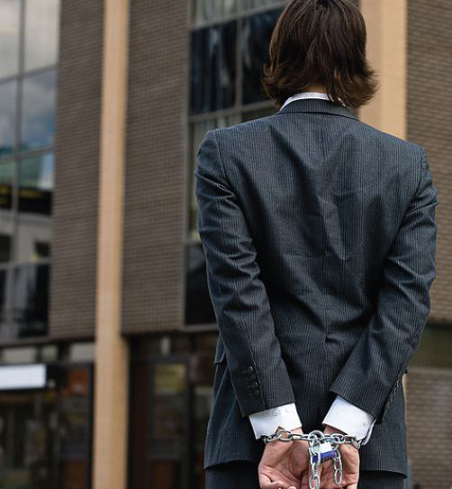 Man in suit with hands chained behind his back. A padlock is visible on the chains.